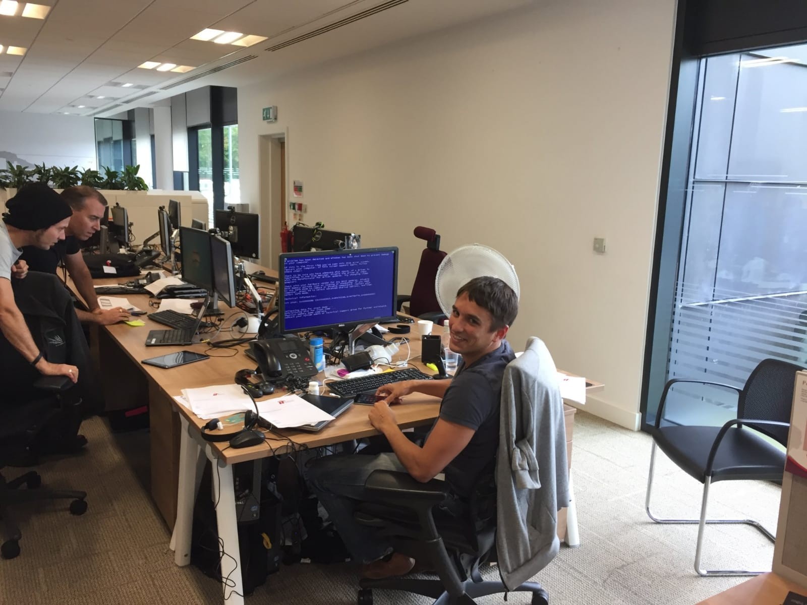 Jamie at his Imperial Tobacco desk with a Blue Screen of Death on the monitor behind him, everyone laughing